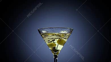 Two olives fall into tall martini glass. Black background