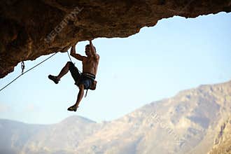 Young man struggling to climb ledge on natural cliff