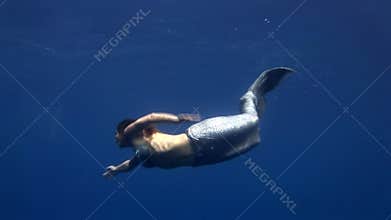 Young girl model underwater mermaid costume on blue background poses in Red Sea.