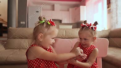Two charming twin sisters pamper each other, playing with their hands together.