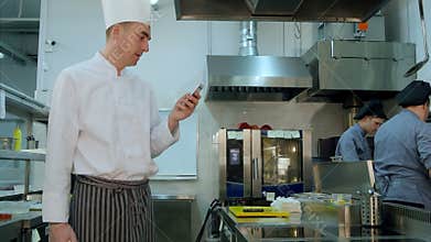 Head cook standing in the kitchen and using his cell phone