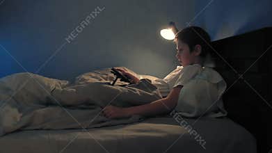 Boy resting in his bed in the evening using his digital tablet