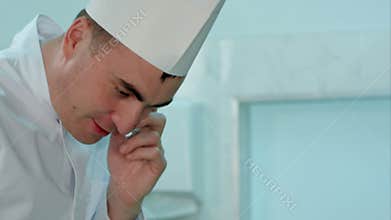 Male chef in white uniform cooking and talking on the phone
