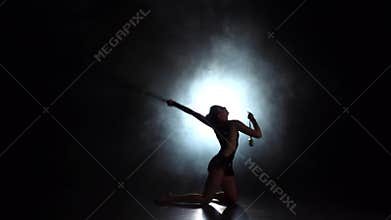 Rhythmic gymnast throws mace up and catches her. Black background. Light rear. Silhouette. Slow motion