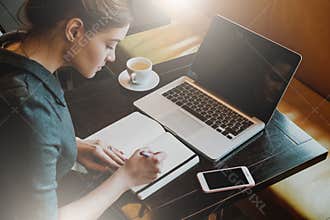 Young business woman in gray dress sitting at table in cafe and writing in notebook.
