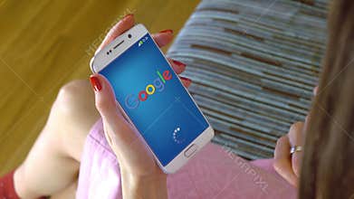 Young woman holding a cell phone with loading Google mobile app. Conceptual editorial 4K clip