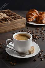Cup of fresh coffee with croissants on dark background