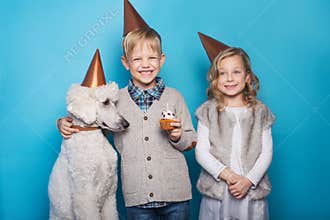 Little beautiful girl and handsome boy with dog celebrate birthday. Friendship. Family. Studio portrait over blue background