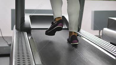 Female legs walking and running on treadmill in gym. Young woman exercising during cardio workout. Feet of girls in