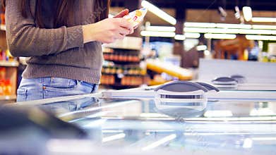 Female hands opening glass door in the refrigerated section at the supermarket and choosing ice cream. Young woman