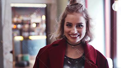 Young hipster girl with casual outfit looks right in the camera and smiles happily. Stylish look, red coat, light makeup