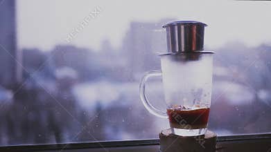 Coffee drips drops in a cup on a background of the urban landscape outside the window. Brew coffee in Vietnamese. Slow