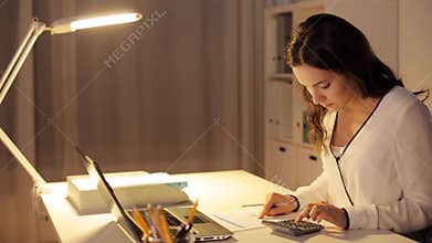 Woman with calculator and papers at night office