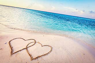 Two hearts drawn on sand of a tropical beach at sunset.