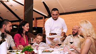Chef comes out to the customers of the restaurant, serves grilled meat, family in restaurant, great food and alcoholic