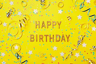 Happy birthday greeting text decorated with confetti and serpentine on yellow background top view. Flat lay style.