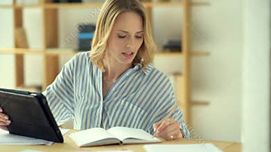 Joyful blonde lady writing down information while browsing internet