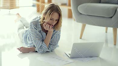 Pensive female freelancer working with documents while lying on floor