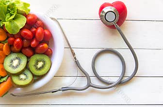 Diet and weight loss for healthy care with medical stethoscope, with red heart and fresh vegetable salad and healthy food on woode