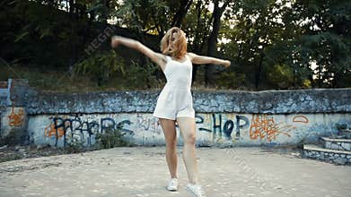 Young Asian woman dancing modern choreography in city park, outside. City ruins and graffiti Variety
