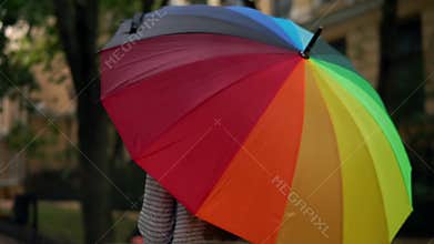 Closeup view of an open spinning colourful rainbow umbrella in female hands. Slowmotion shot