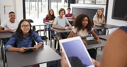 Teacher uses tablet in high school class, over shoulder view