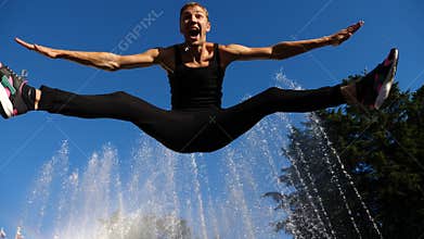 A young happy guy dancing modern ballet and wacking on a background of a fountain in a summer park. Slow-mo