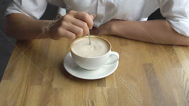 A young beautiful woman drinking coffee in a cafe. Hand of girl stiring sugar in coffee close up