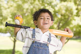 Young boy holding baseball bat outdoors smiling