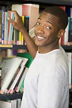 Male college student reaching for a library book