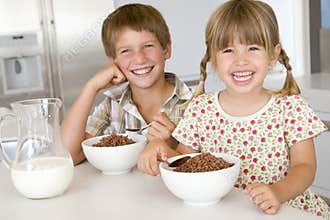 Two young children in kitchen eating cereal
