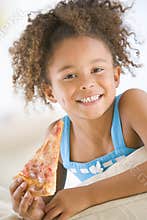 Young girl eating pizza slice in living room