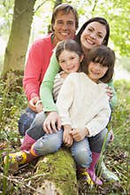Family outdoors in woods sitting on log smiling