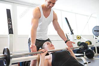 Fitness Trainer Assisting Woman Lifting Barbell