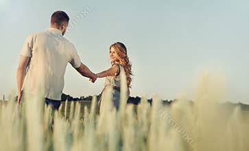 stunning happy young couple in love posing in summer field holding hands