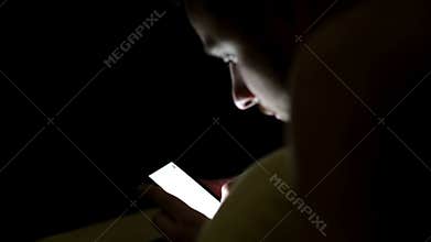 Young man using smartphone in the bed under blanket by night