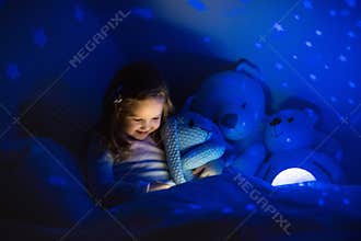 Little girl reading a book in bed