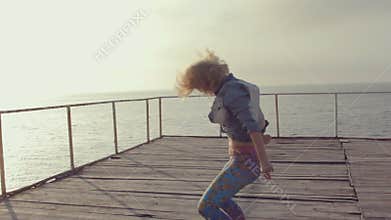 Girls in bright leggings professionally dancing modern dance on a wooden pier near the sea at sunset