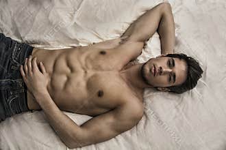 Shirtless male model lying alone on his bed