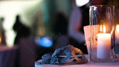 Masquerade gold venetian mask lies on a table in a nightclub during a costume party, white candle burning in a glass cup