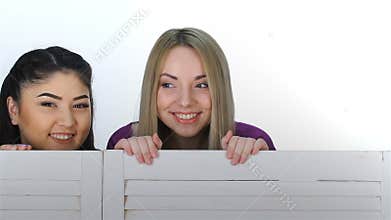Three girls look out from behind a folding screen