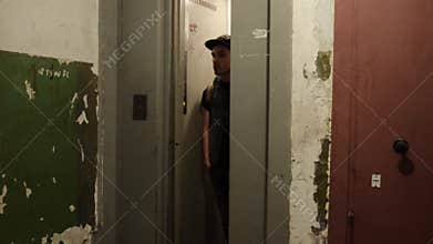 Man in cap with backpack walk out narrow elevator. Old house. Ragged walls