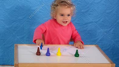 Adorable toddler girl with curly hair painting with crayons on paper sitting