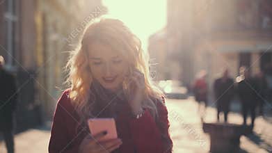 Business woman sms texting using app on smart phone. Attractive girl in red coat walking in the sunshine old city.