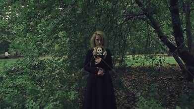 Stylized shot creepy white faced woman with a doll in the grass in the woods