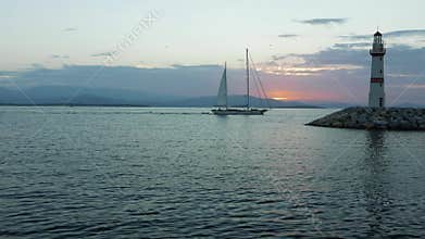Sailling boat coming to the marina with silhouette of lighthouse and sunrise on the background. 4k