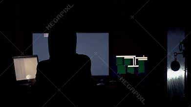 Hacker in hood cracking code using computers in dark room