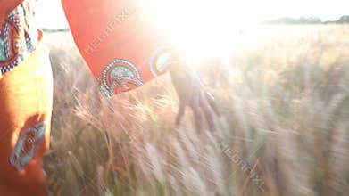 African woman in traditional clothes walking with her hand on a field of crops at sunset or sunrise