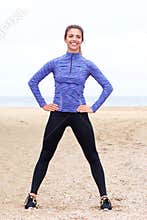 Smiling athlete standing on beach with hands on hips