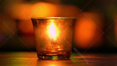 Candle in a glass stay on wooden table in blues music bar. Blurred backround. Bokeh. Colored illumination. Slow motion